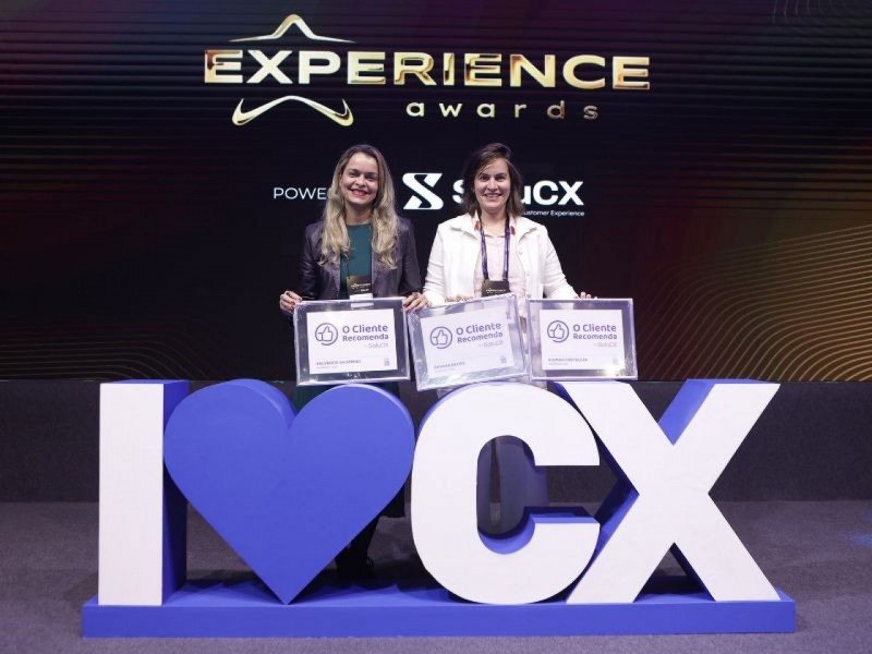 A foto mostra duas mulheres representantes do Grupo JCPM recebendo as certificações dos shoppings premiados com o Experience Awards.