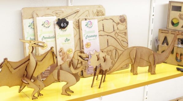 Dinossauros mont&aacute;veis de madeira sobre uma prateleira amarela.