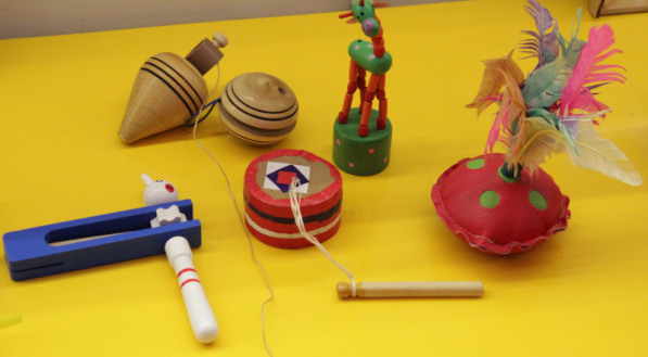 Brinquedos cl&aacute;ssicos, como pe&atilde;o, ioi&ocirc; e peteca, dispostos em uma mesa.