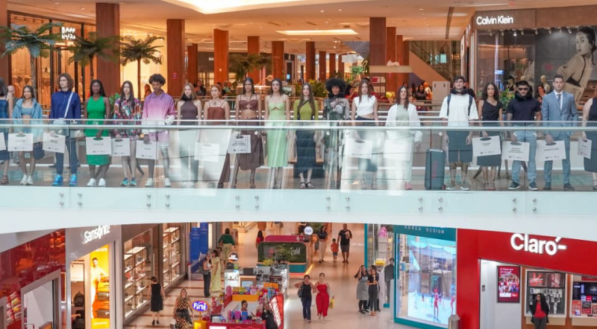 V&aacute;rios modelos est&atilde;o em fila, parados em uma passarela de vidro. Eles vestem uma variedade de looks coloridos de primavera/ver&atilde;o.