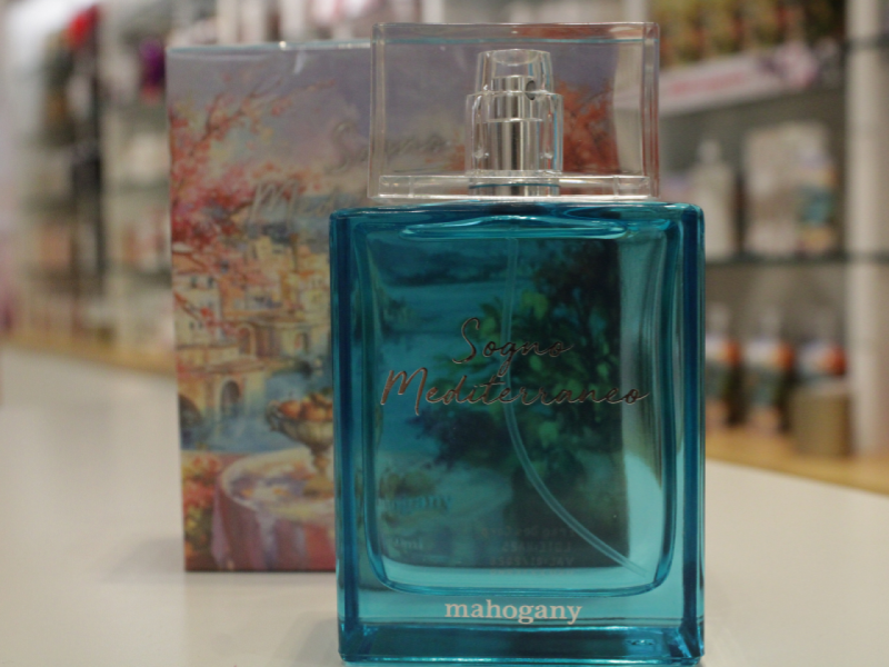 A imagem mostra o perfume "Sogno Mediterraneo" da Mahogany, de cor azul-água, em primeiro plano. 
