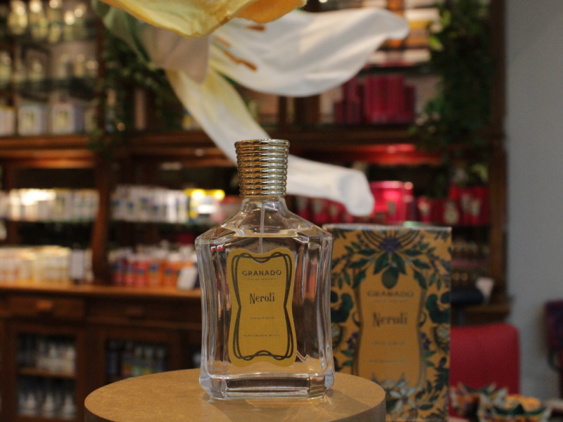 A imagem mostra o perfume  "Neroli" da Granado, exibido sobre um pedestal em uma loja, com sua caixa decorada ao fundo.