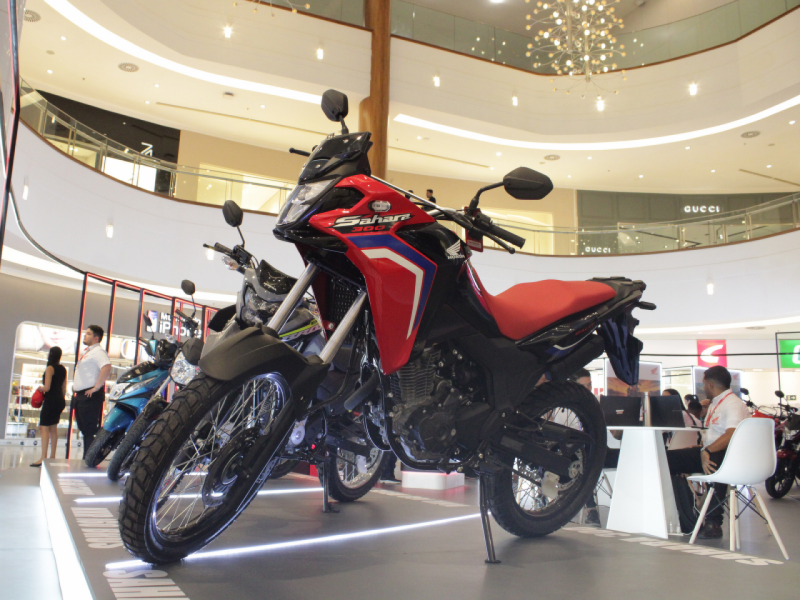 A imagem mostra um close-up de uma moto Honda Sahara 300 vermelha e preta, em exibição. 