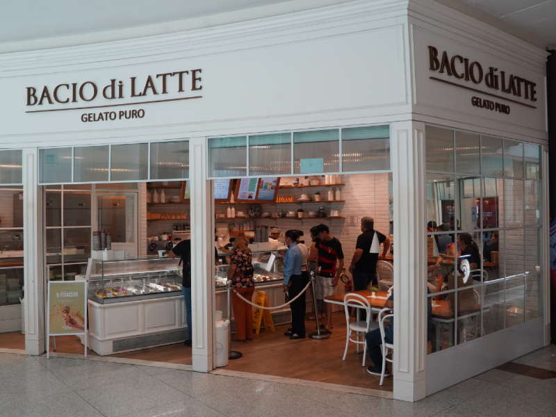 A imagem mostra a fachada da Bacio di Latte, com um design limpo e elegante em branco. 
