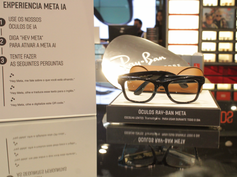 Ã?culos Ray-Ban preto com lentes transparente, vistos de perto em um expositor branco e preto.