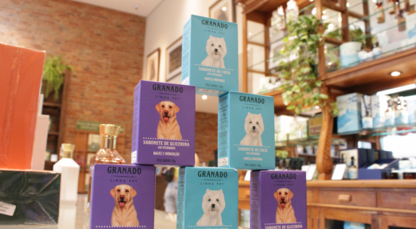 Uma pilha de sabonetes pet da Granado, em caixas roxas e azuis claras, com fotos de um Labrador e um Westie. Eles estão em um balcão de loja.