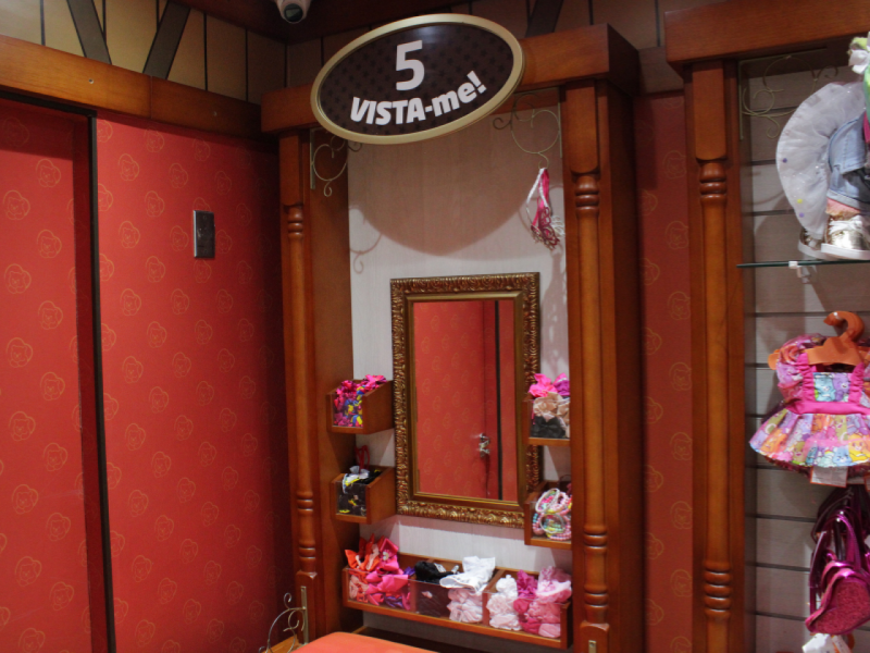 A imagem mostra a etapa 5 (vista-me!), onde o cliente escolhe roupas e acessórios em frente a um espelho para vestir a pelúcia personalizada.