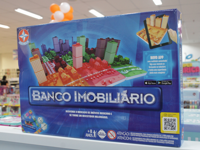 A imagem mostra a caixa do jogo "Banco Imobiliário" da Estrela, destacando um cenário de cidade colorida.