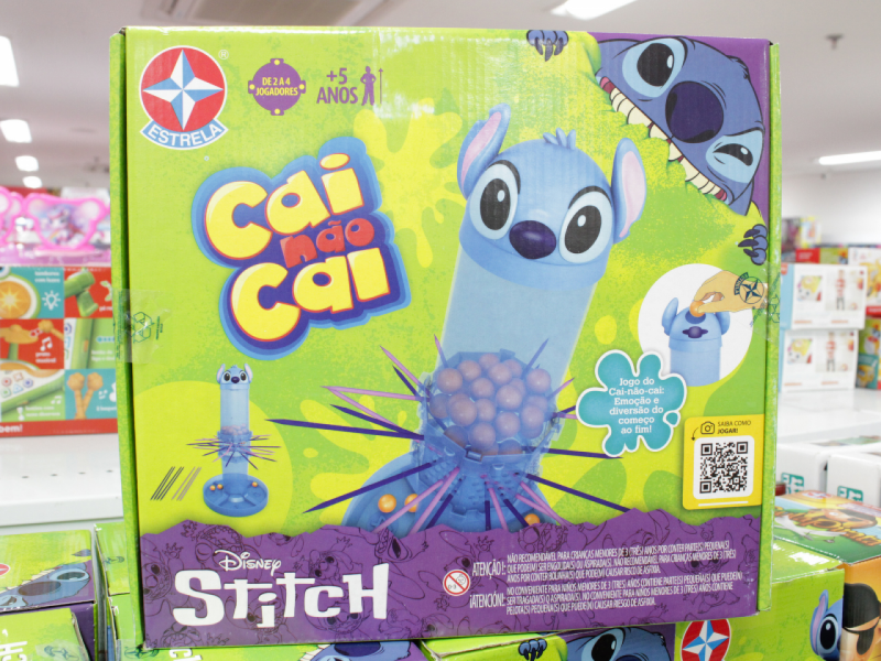 A imagem mostra a caixa do jogo "Cai Não Cai Disney Stitch" da Estrela, apresentando o personagem azul Stitch no design do jogo de habilidade.