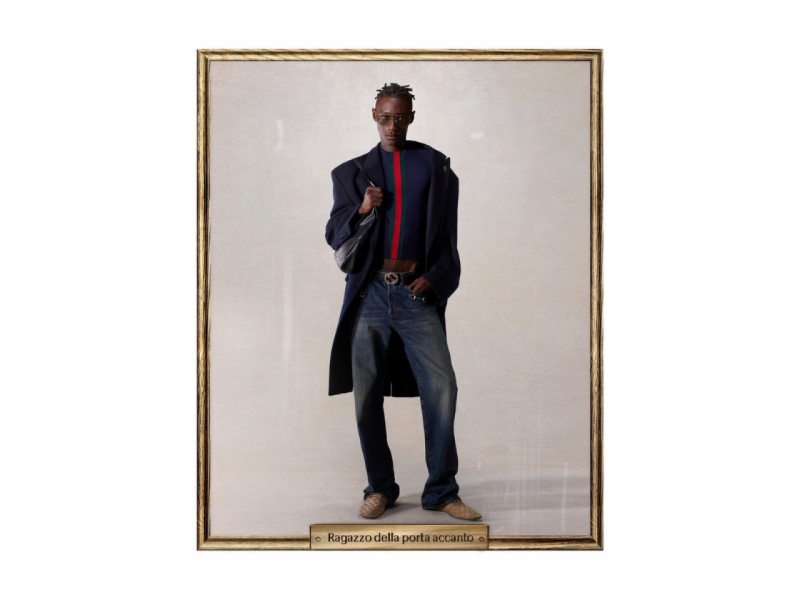 A imagem mostra o modelo Ragazzo della porta accanto da nova coleção da Gucci, combinando casaco longo, suéter listrado, jeans e o cinto clássico da marca.