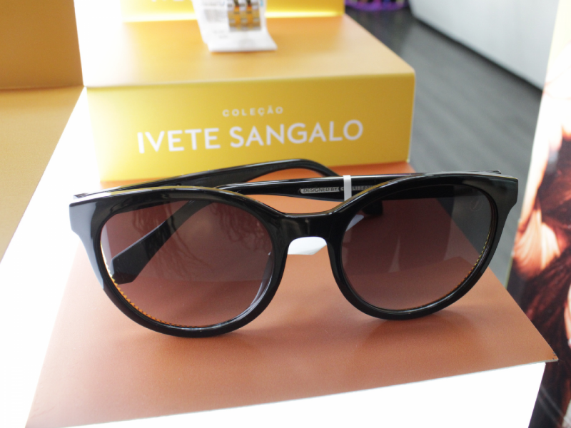 Óculos de sol de aro preto estilo gatinho, com lentes marrons, sobre uma base laranja.