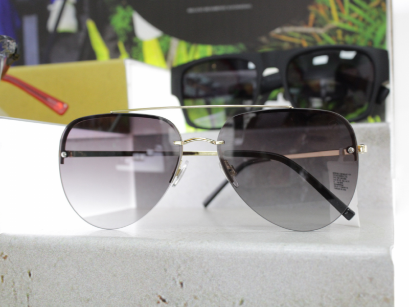 Óculos de sol estilo aviador, com lentes grandes em degradê cinza e armação dourada fina.
