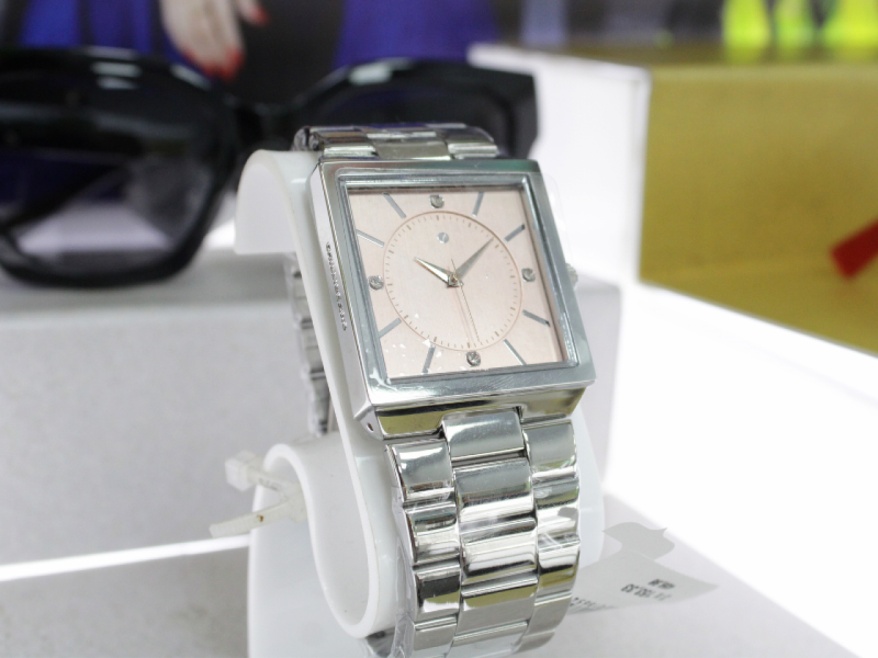 Relógio de pulso prateado com pulseira de metal e mostrador quadrado em tom pêssego, com pequenos detalhes de diamante.