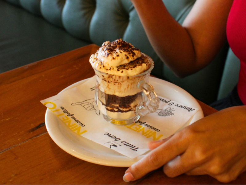 A imagem mostra uma pessoa comendo o clássico Tiramisù, sobremesa do menu de jantar.