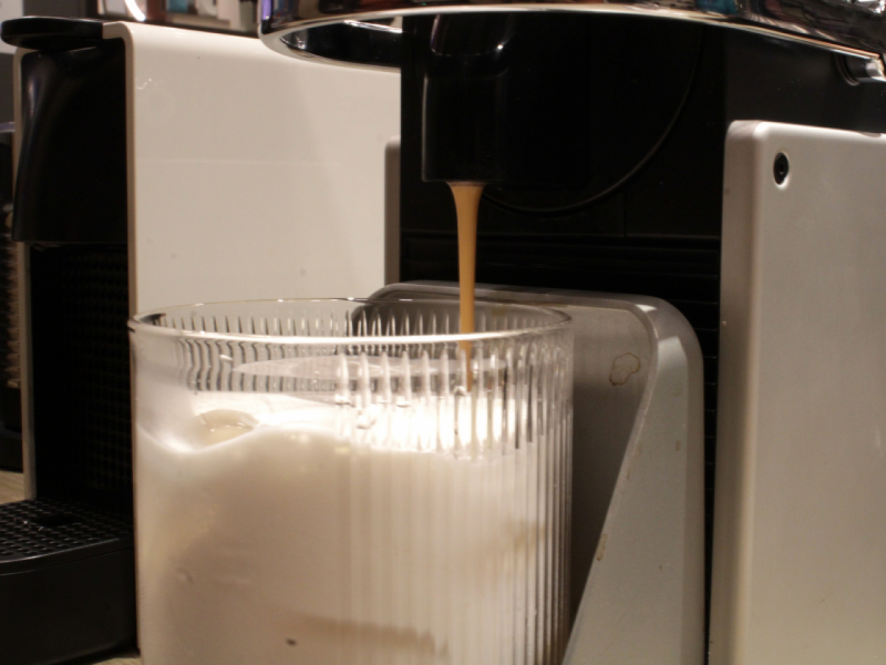 A imagem mostra o café sendo derramado de uma máquina Nespresso diretamente para um copo alto com leite e gelo. A imagem mostra o café sendo derramado de uma máquina Nespresso diretamente para um copo alto com leite e gelo.