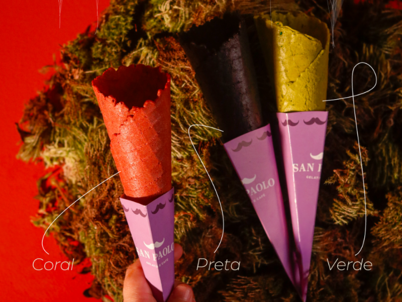 A imagem mostra três casquinhas de sorvete da San Paolo com sabores ou cores especiais: Coral, Preta e Verde, com embalagens personalizadas de bigode.
