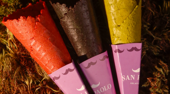 A imagem mostra três casquinhas de sorvete da San Paolo com sabores ou cores especiais: Coral, Preta e Verde, com embalagens personalizadas de bigode.