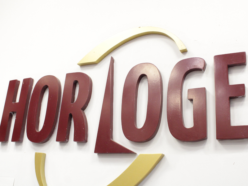 A imagem mostra a logo da Horloge nas cores vinho e amarelo