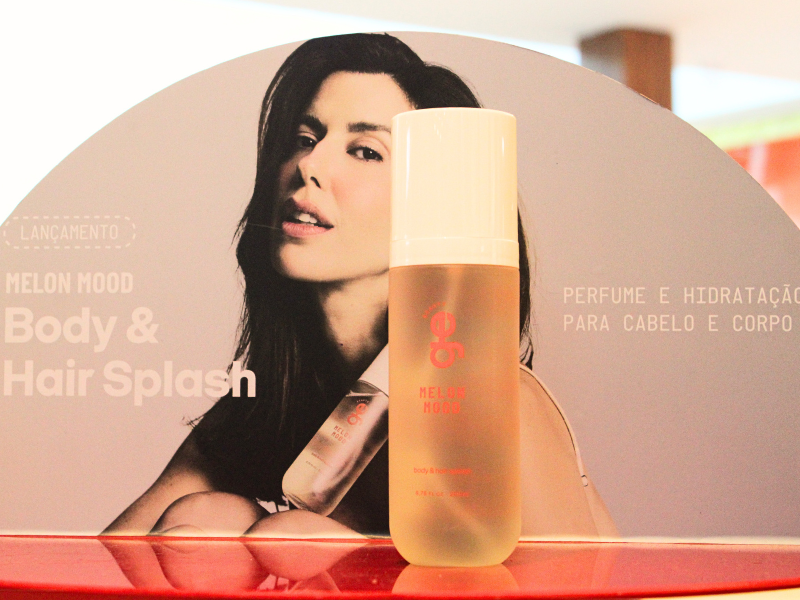 A imagem um frasco de Body e Hair Splash num display com foto de Camila Coutinho ao fundo 