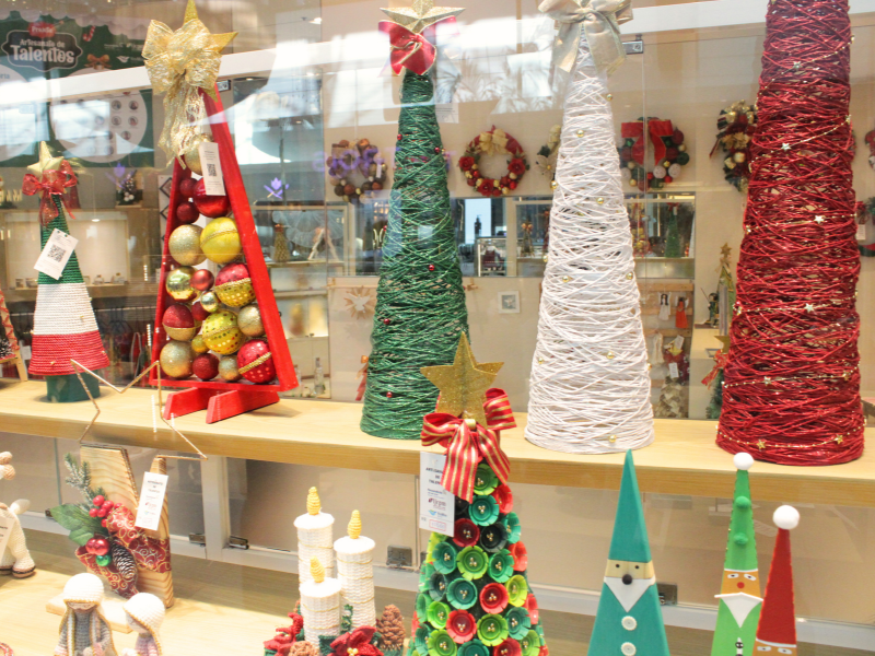 A vitrine mostra uma variedade de árvores de Natal decorativas em formato cônico, feitas com fios coloridos (vermelho, branco e verde).