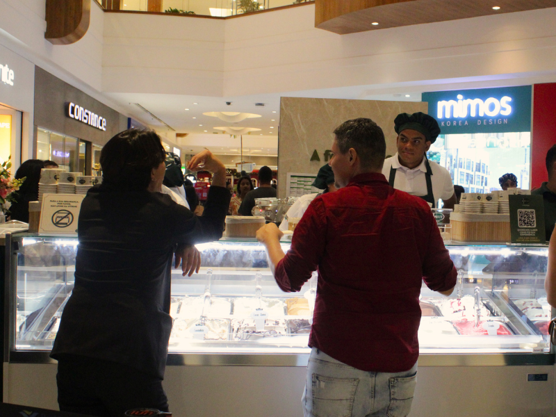 Clientes em frente ao balcão de vidro da sorveteria, observando e escolhendo os sabores de gelato no shopping.