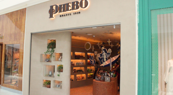 Fachada da loja Phebo, com o letreiro em relevo e nichos decorativos com plantas na entrada. O interior apresenta um balcão redondo e decoração temática iluminada.