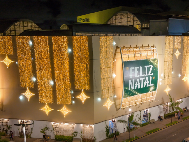 Close-up noturno de uma das laterais do edifício, coberta por cortinas de luzes douradas e grandes estrelas. Um painel com a mensagem 
