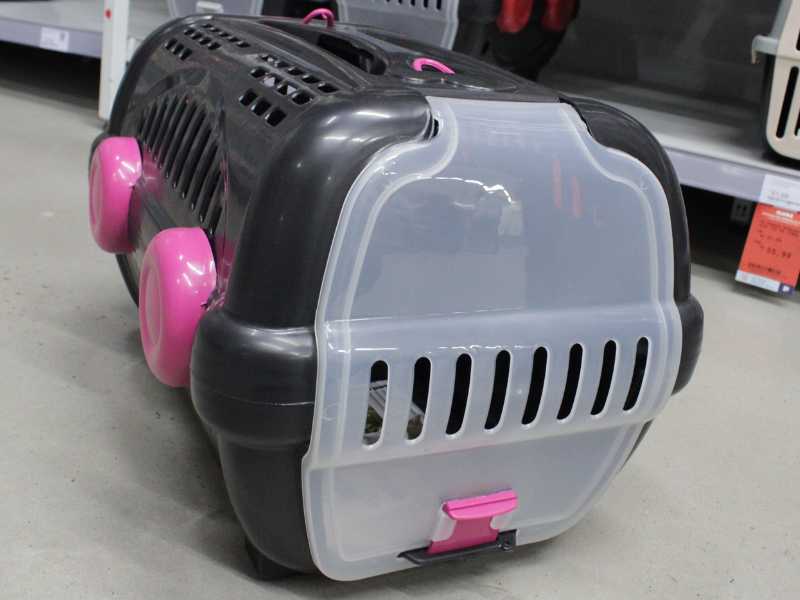 Caixa de transporte de plástico rígido para animais de cor cinza escura e porta frontal de plástico branco leitoso, com detalhes em rosa choque nas travas.