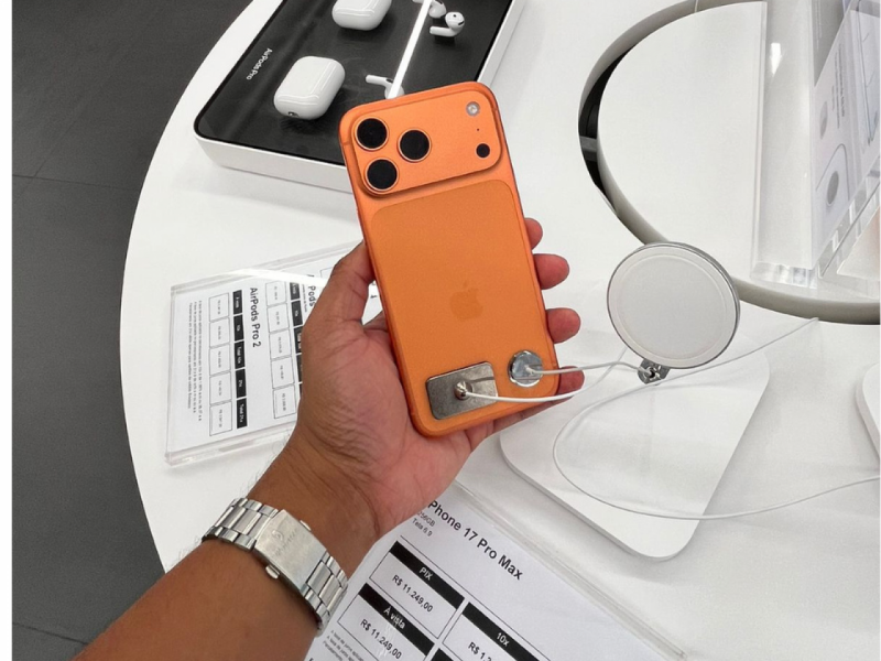 Mão segurando o novo iPhone 17 pro max na cor laranja, mostrando a parte traseira.