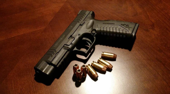 Foto de uma pistola ao lado de balas para arma de fogo. Imagem ilustrativa para falar de assassinato