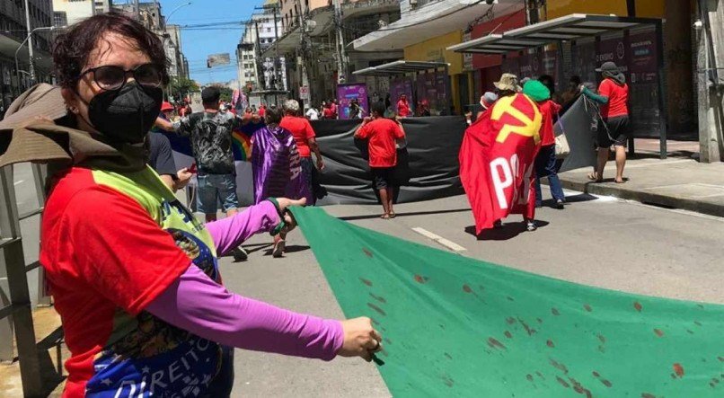 Membro da coordena&ccedil;&atilde;o do ato, Roberta Almeida segurava bandeira do Brasil com manchas vermelhas para lembrar v&iacute;timas da covid-19