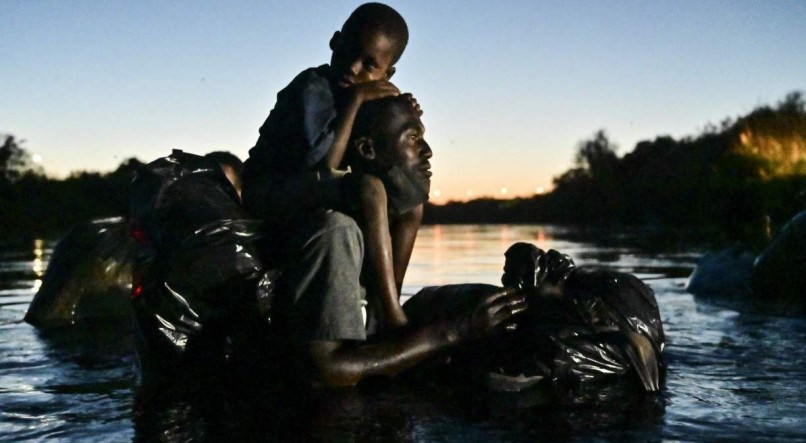 TRAVESSIA Homem carrega crian&ccedil;a enquanto  cruza o rio na fronteira