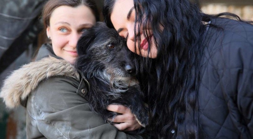 Mulheres abraçam um cachorro no abrigo "Home for Rescued Animals" na cidade de Lviv, no oeste da Ucrânia, em 26 de março de 2022