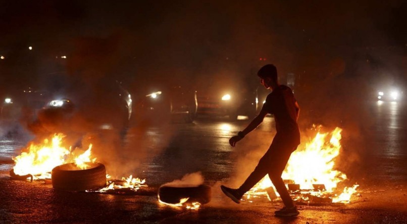 CONFLITO Jovem palestino chuta um pneu em chamas em protesto contra os ataques aéreos israelenses em Gaza