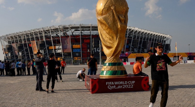 QUEM LEVA A TAÇA PARA CASA? Torcedores tiram fotos com taça gigante colocada na frente do estádio em Doha. Será a primeira copa disputada no Oriente Médio