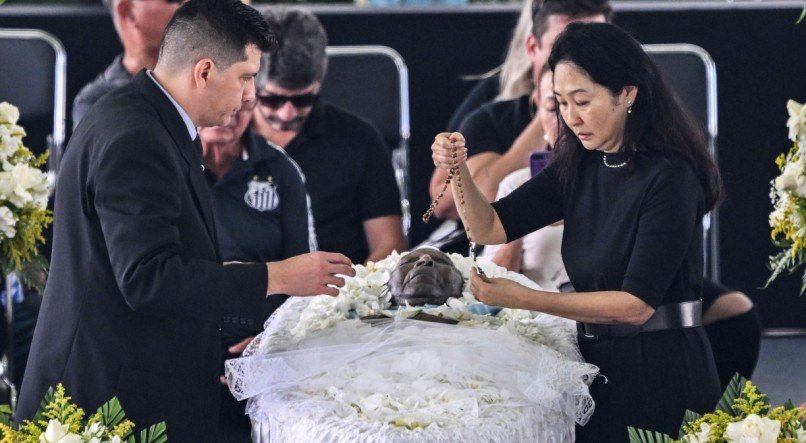 Márcia Aoki segurando um terço ao lado do caixão de Pelé