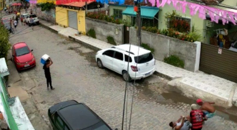 O vídeo mostra um grupo de foliões passando pela rua e, segundos depois, três criminosos se aproximando de dois homens