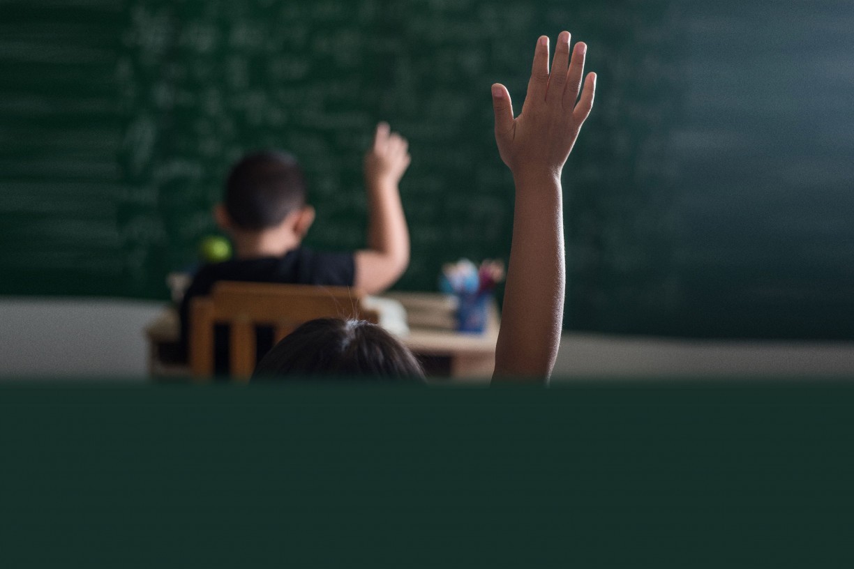 Crianças em sala de aula levantando um braço