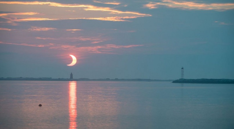 A partial solar eclipse is seen as the sun rises behind the Delaware Breakwater Lighthouse, Thursday, June 10, 2021, at Lewes Beach in Delaware. The annular or “ring of fire” solar eclipse is only visible to some parts of Greenland, Northern Russia, and Canada. Photo Credit: (NASA/Aubrey Gemignani)