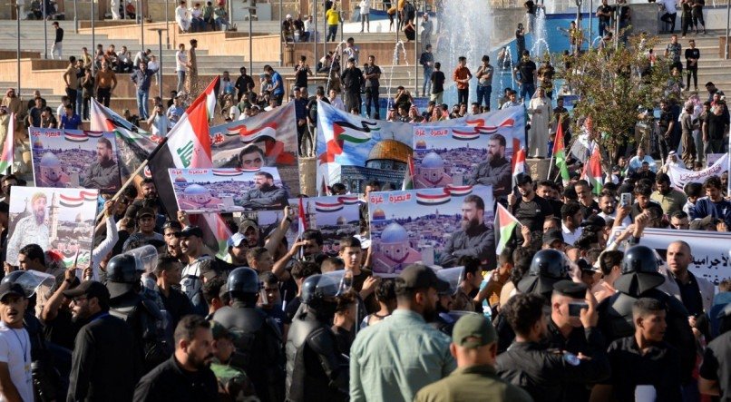 As pessoas levantam bandeiras e estandartes enquanto se manifestam em apoio aos palestinos em Gaza e na Cisjordânia, na cidade iraquiana de Mosul, neste sábado (14)