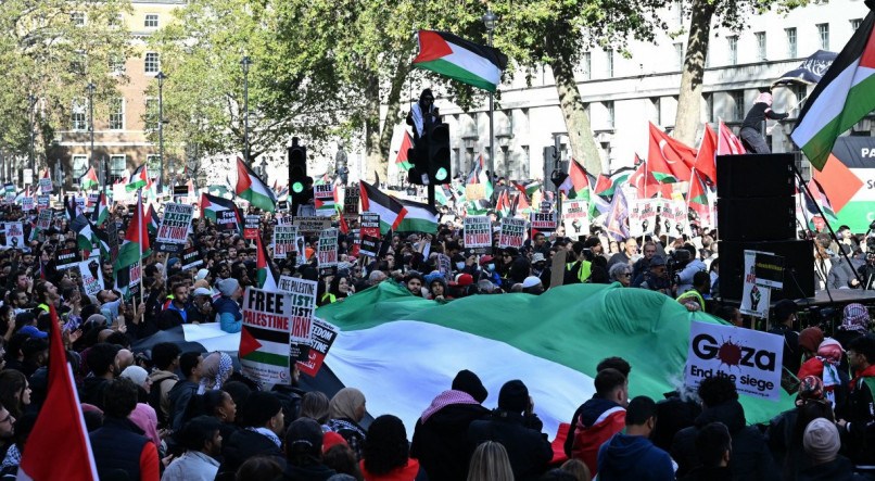 Manifestantes carregam cartazes e uma grande bandeira palestina ao longo de Whitehall durante uma 'Marcha pela Palestina', parte de uma manifestação nacional pró-Palestina, em Londres, neste sábado (14) 