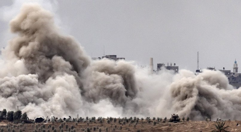 Foto deste domingo (12) de uma posição ao longo da fronteira com a Faixa de Gaza, no sul de Israel, mostra um tanque israelense e uma nuvem de fumaça em erupção durante bombardeio