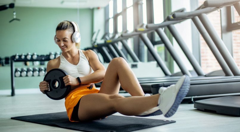 Smiling sportswoman doing abdominal exercise with weight plate at health club.