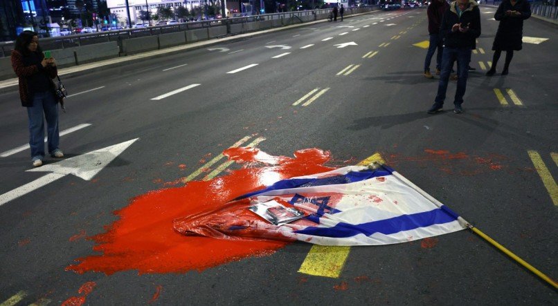 Bandeira israelense coberta de tinta vermelha enquanto parentes e apoiadores de reféns mantidos por militantes palestinos manifestam-se em frente ao Ministério da Defesa de Israel em Tel Aviv, em 15 de dezembro de 2023