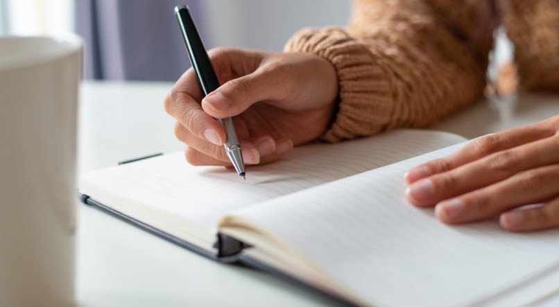 Close-up of woman sitting at table and planning schedule. Unrecognizable lady making notes in diary. Tasks concept