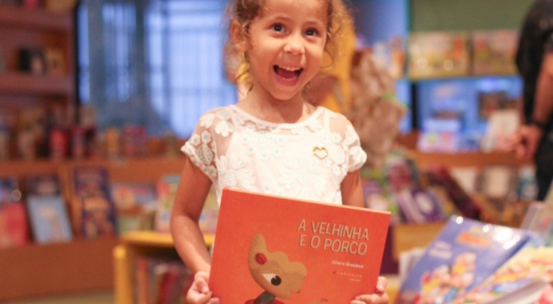 Criança com o livro de Clara Haddad nas mãos, em evento na Livraria Jaqueira