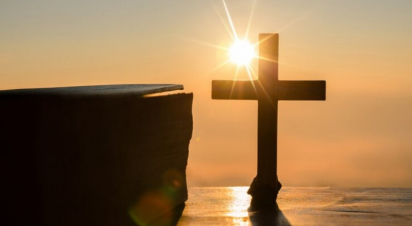 Imagem de uma cruz ao p&ocirc;r do sol, remetendo &agrave;s festas crist&atilde;s da P&aacute;scoa