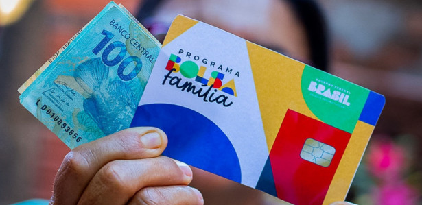 Imagem ilustrativa de uma mulher segurando o cartão do Bolsa Família e notas de dinheiro