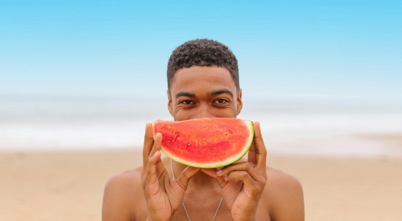 Homem segurando melancia na praia.