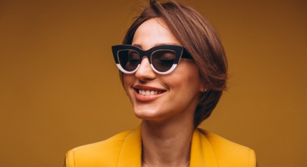 Imagem: Mulher com roupa amarela, sorrindo para a câmera com óculos. 